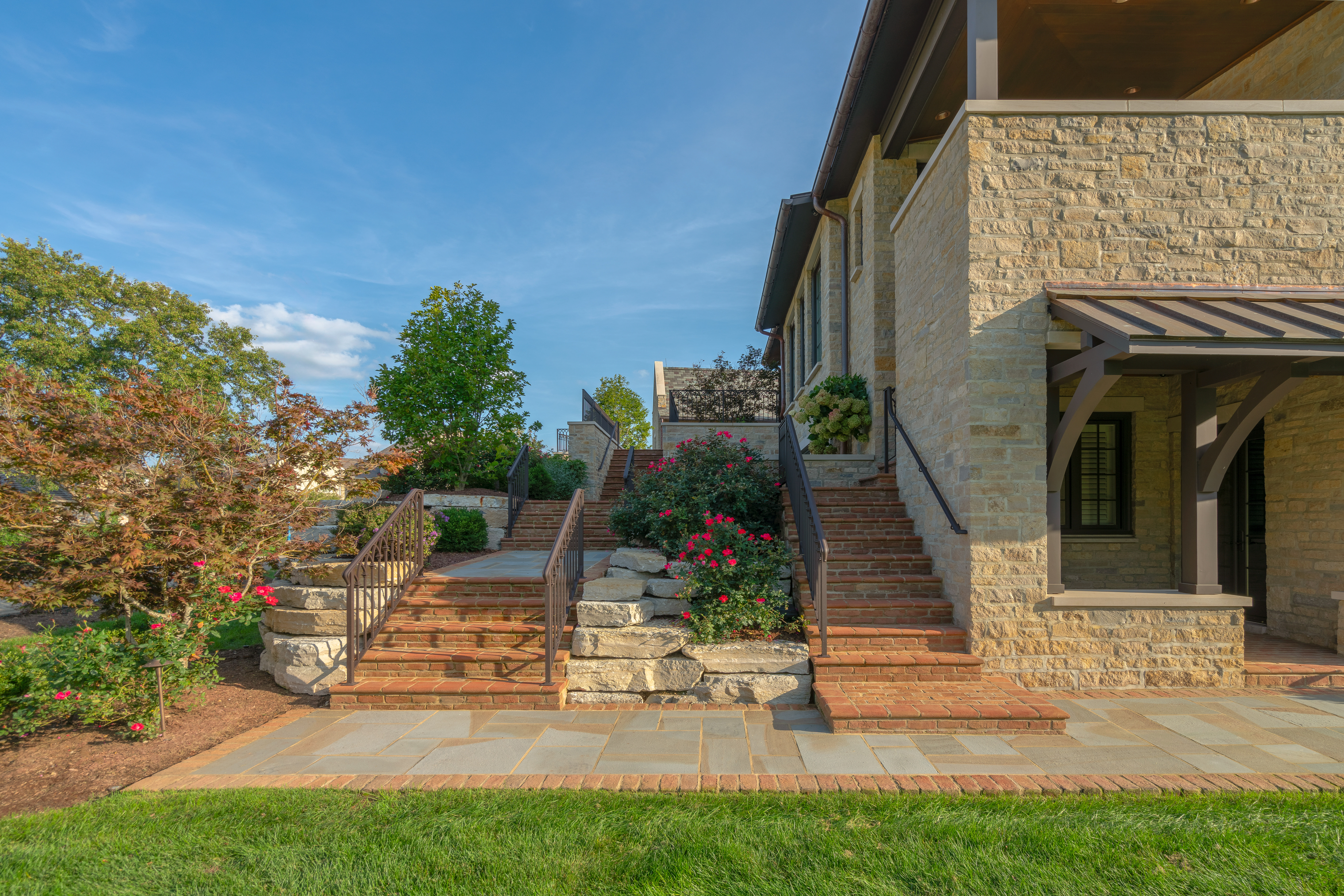 Brick stairs, bluestone landing, and lush plantings surrounding stairs and in between stairs.