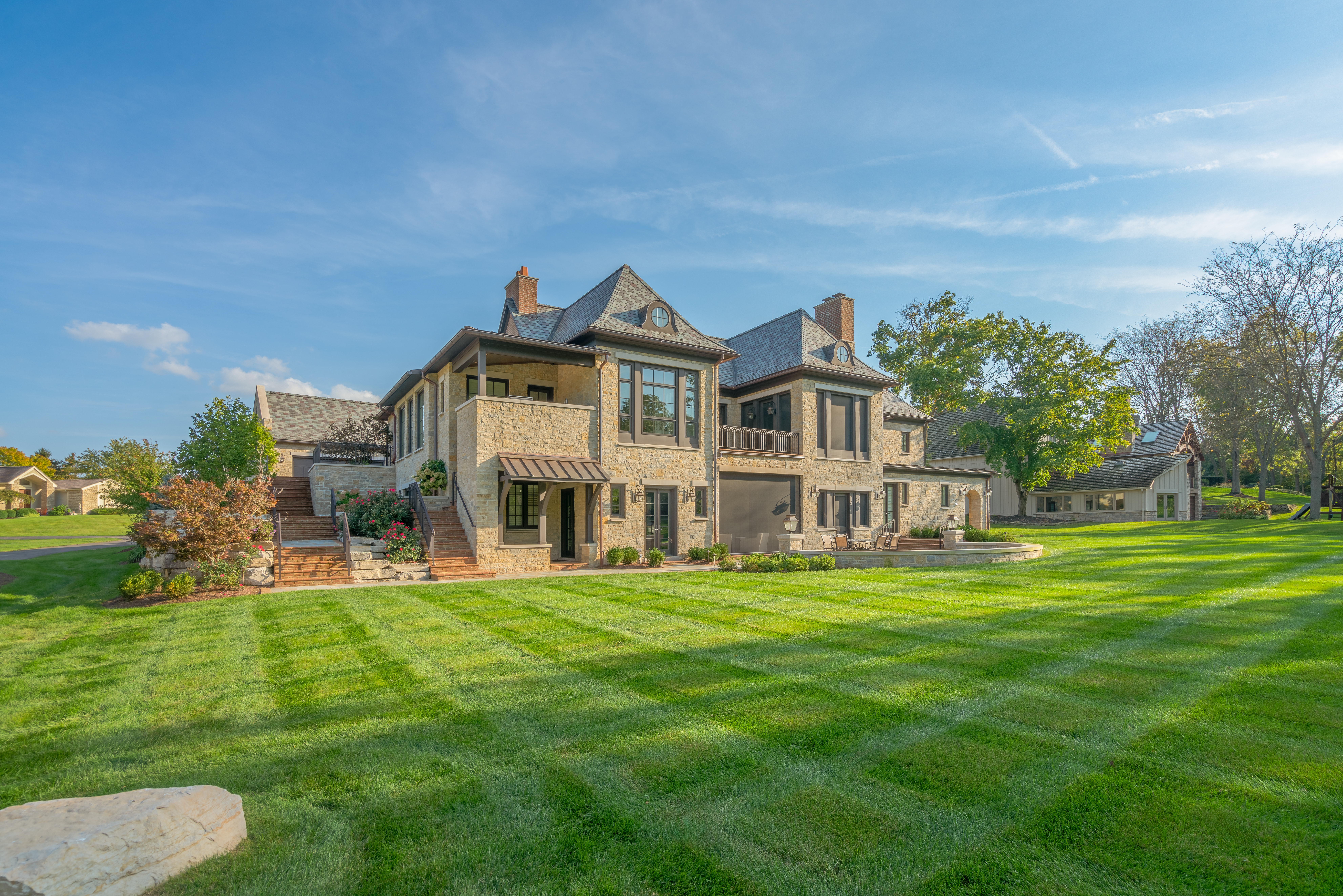 Far view of residential backyard including brick stairs leading to bluestone landing and walkway to patio. Surrounded with plantings and freshly mowed grass.